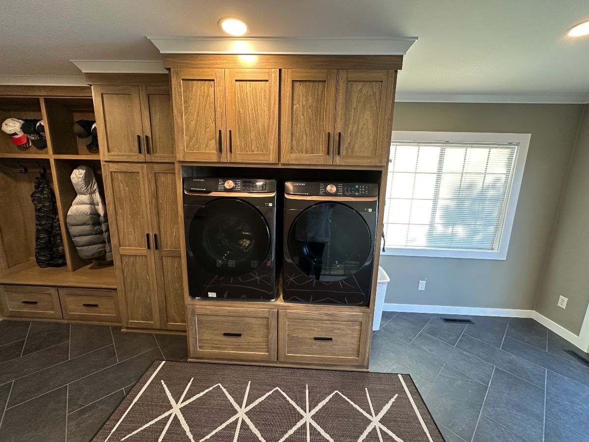 Laundry room with wood cabinets, stacked washer-dryer, tiled floor, and a window with blinds.