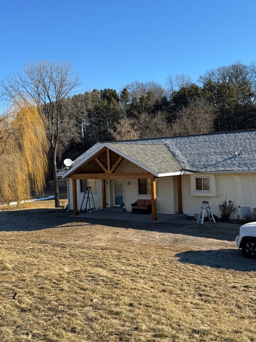 Single-story house with a snowy roof, front porch, and bare yard on a sunny winter day