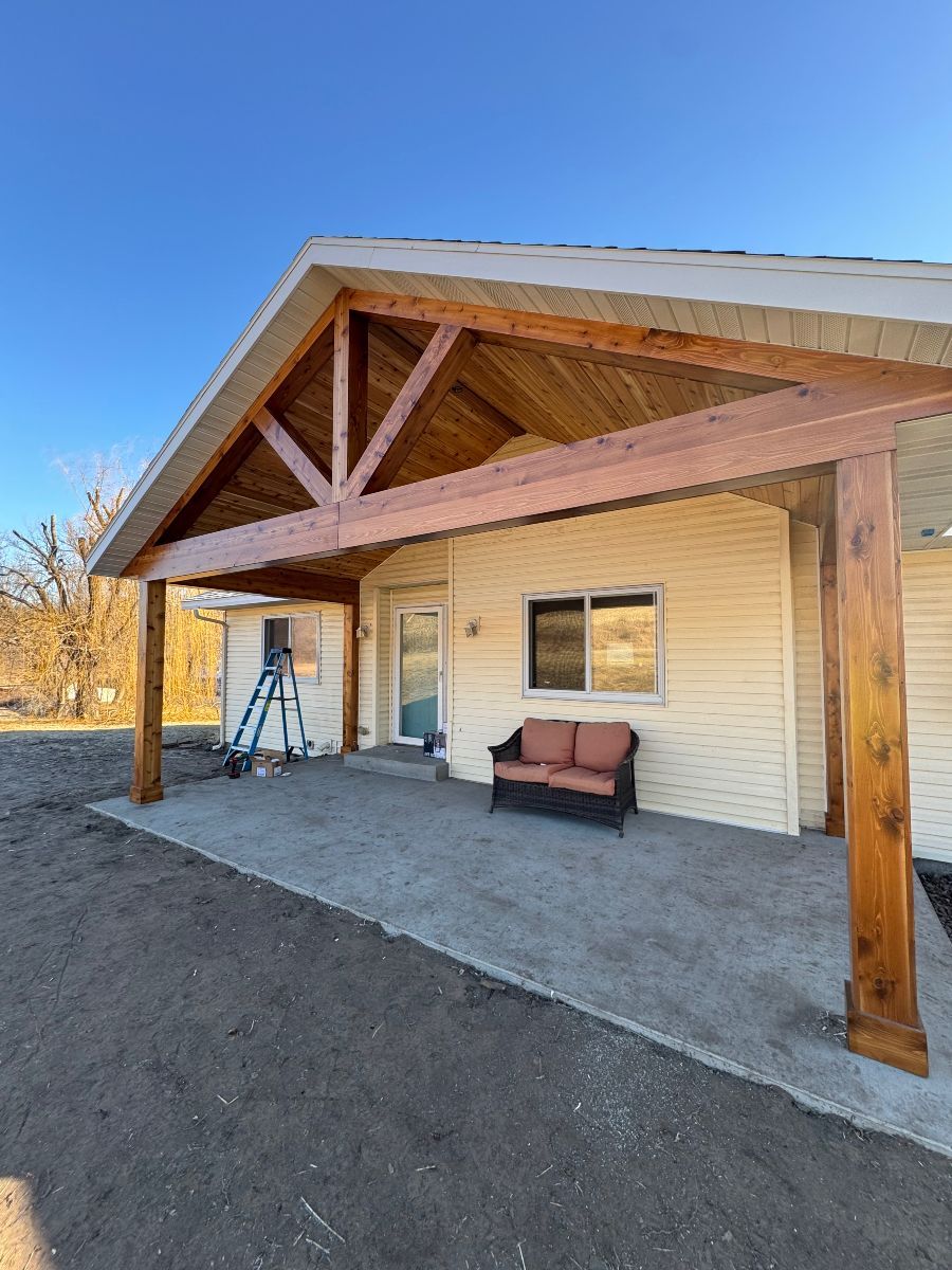 Covered porch with wooden beams, white siding, a window, and a pink loveseat under a clear blue sky.