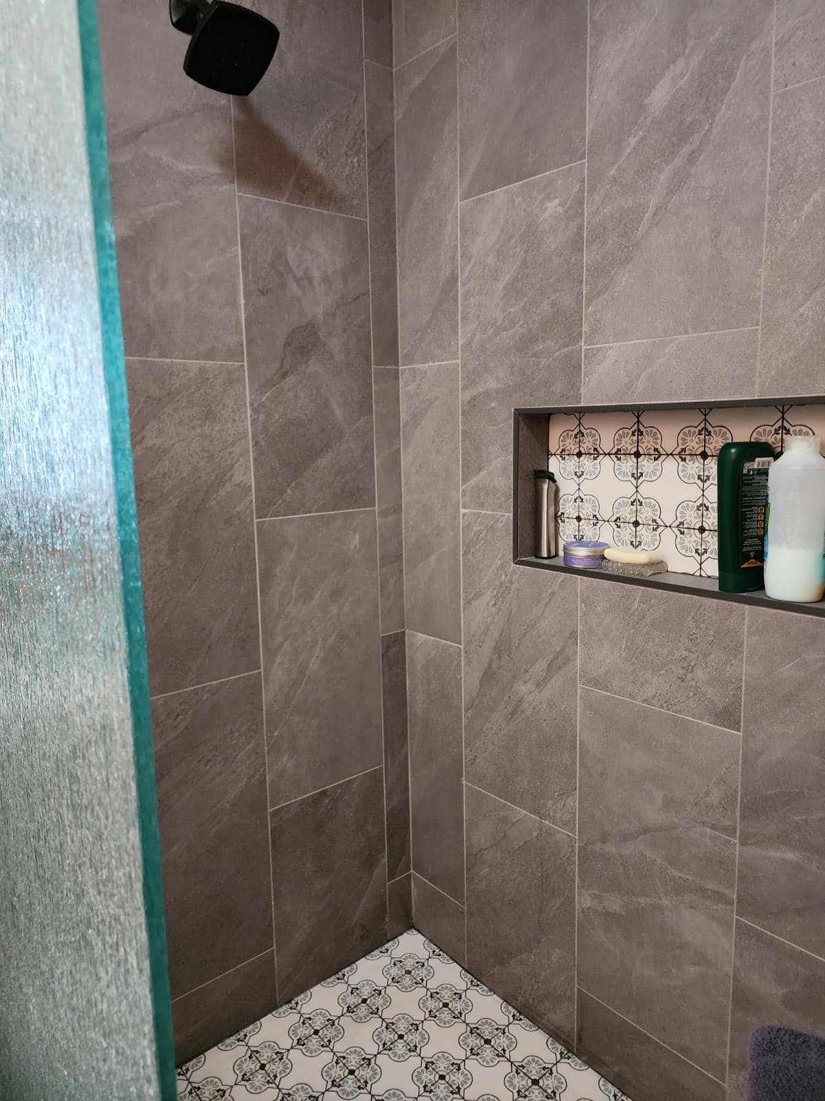 Tiled shower corner with a built-in shelf holding toiletries and a black showerhead above.