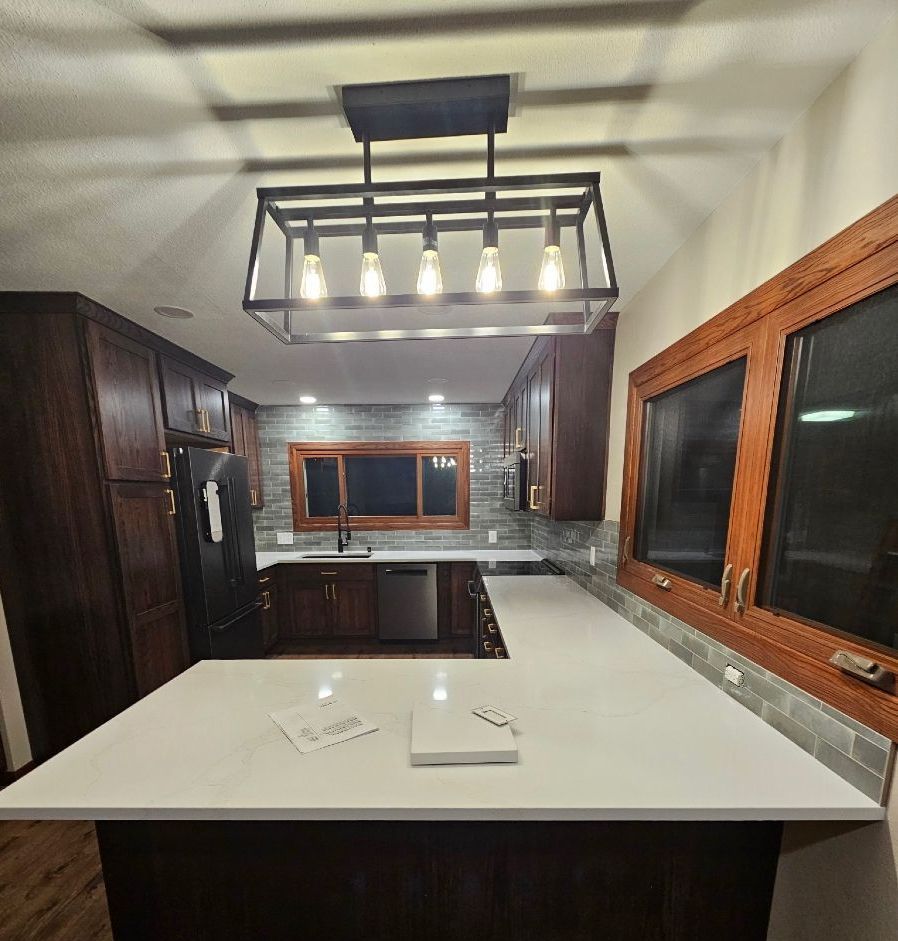 Modern kitchen with white island, dark wood cabinets, large windows, and hanging light fixture