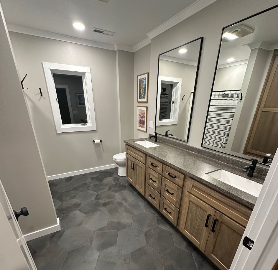 Modern bathroom with double vanity, large mirrors, gray tile floor, and a window near the toilet.