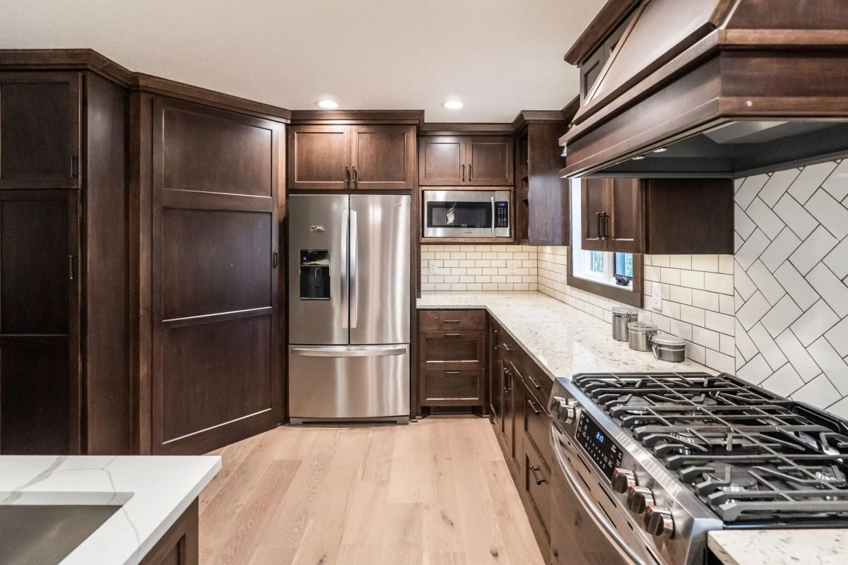 Modern kitchen with dark wood cabinets, stainless steel appliances, light counters, and herringbone tile backsplash