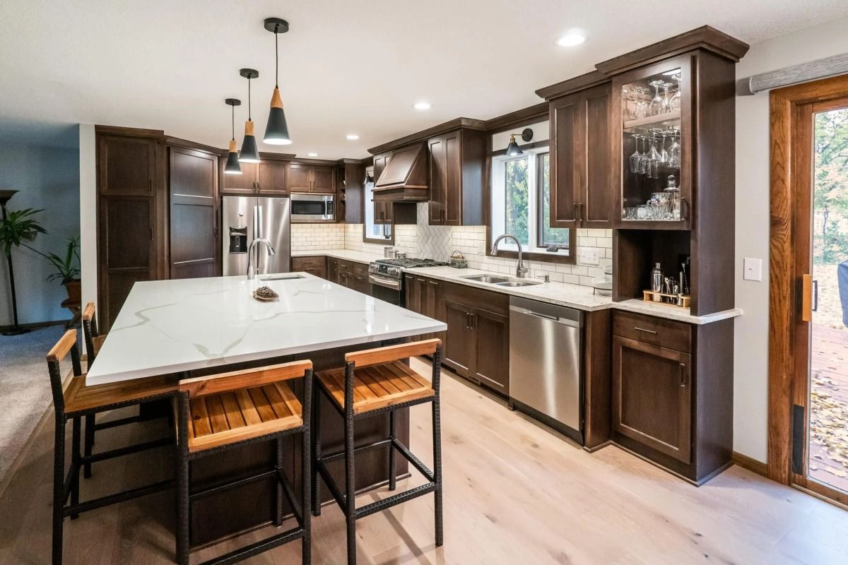 Modern kitchen with large island, dark wood cabinets, pendant lights, and bright windows