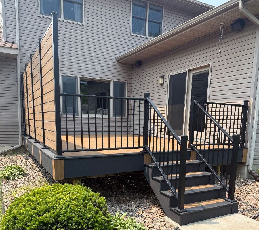 Raised wooden deck with black railings and stairs attached to a brick house exterior