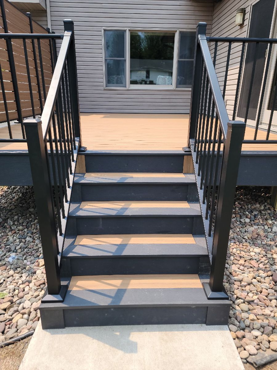 Front steps with black railings leading to a gray house porch and window.