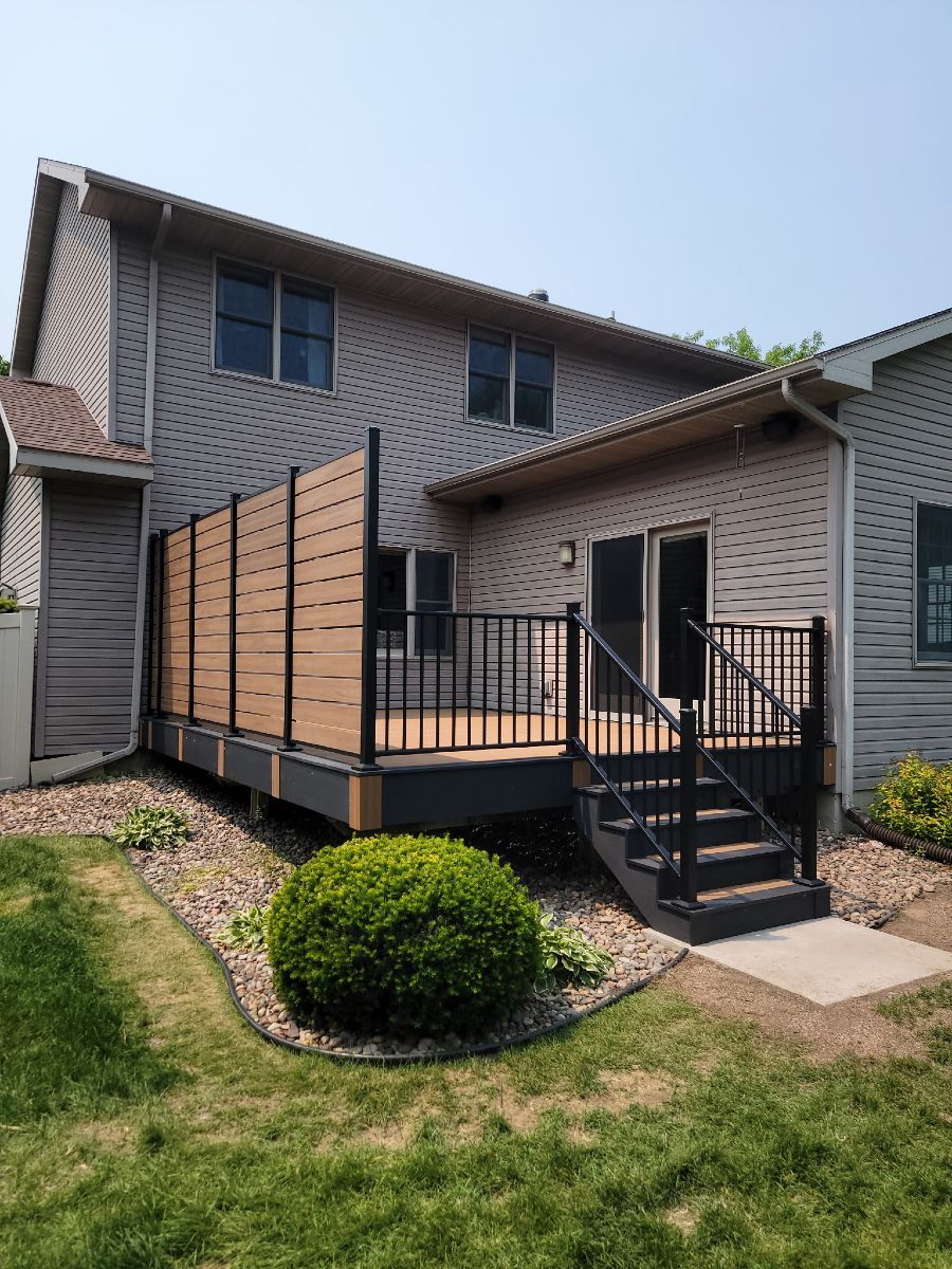 Backyard deck with black railings and steps attached to a two-story house with wood privacy panels.