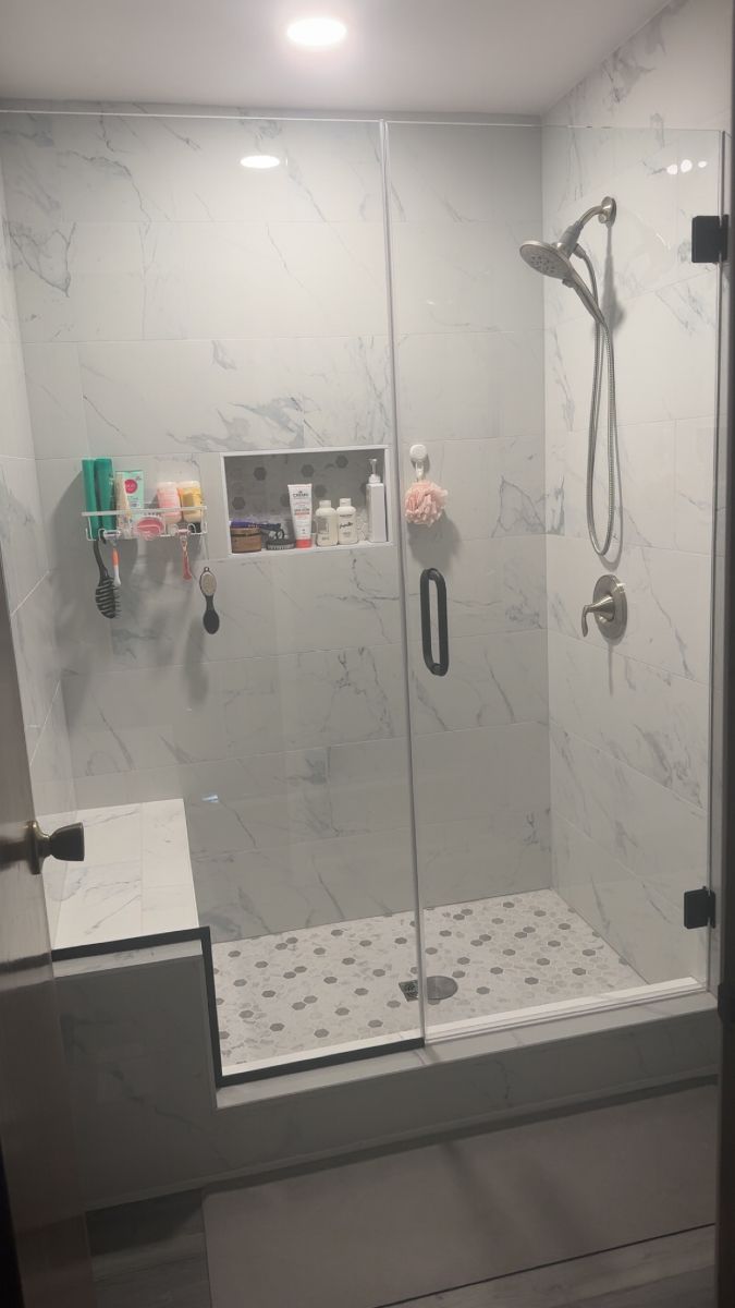 Glass-enclosed walk-in shower with marble walls, built-in niche, handheld shower, and patterned floor tile