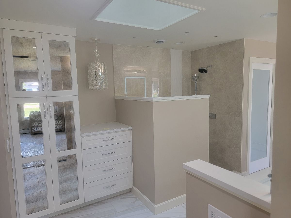 Modern white bathroom with glass shower, vanity drawers, and beige tiled walls