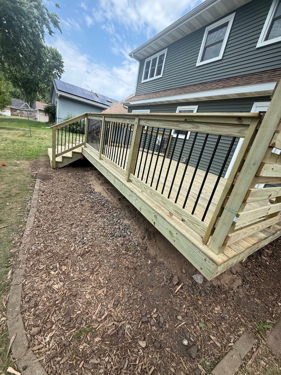 Wooden accessibility ramp with railings beside a house, leading up from a gravel yard.