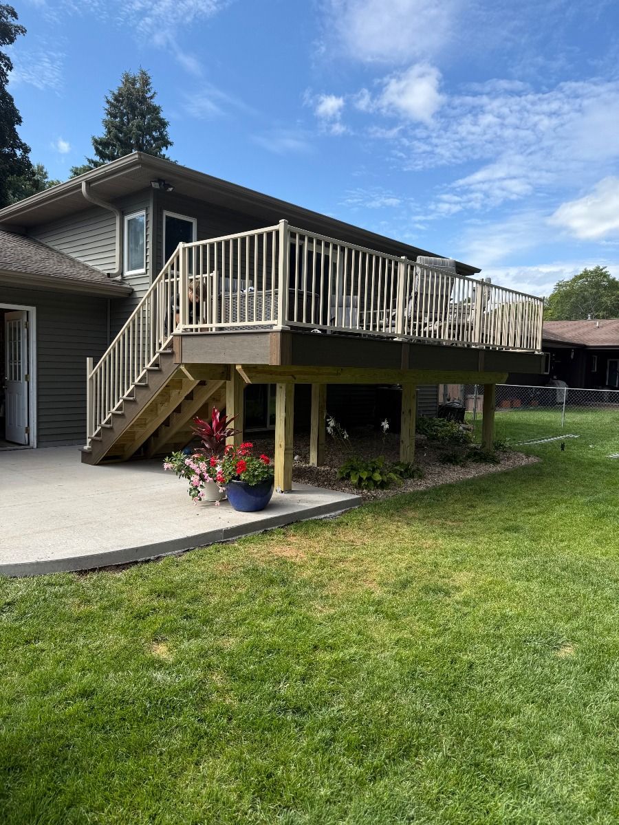 Back deck with stairs on a suburban house, overlooking a grassy yard under a blue sky