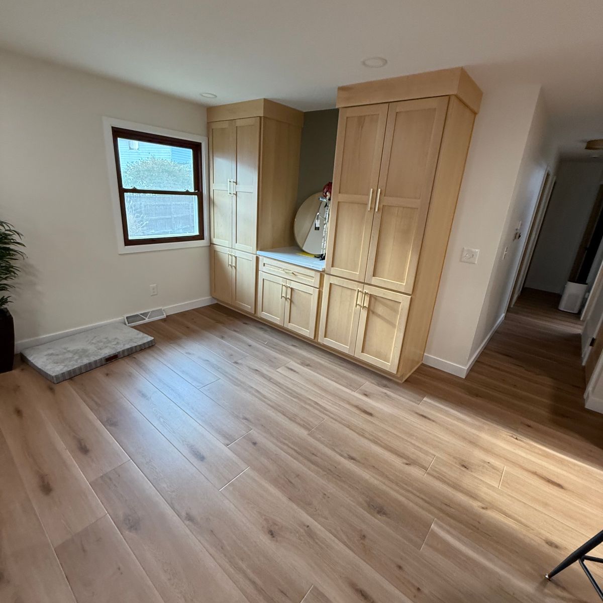 Bright room with light wood flooring, large built-in cabinets, a window, and hallway entrance