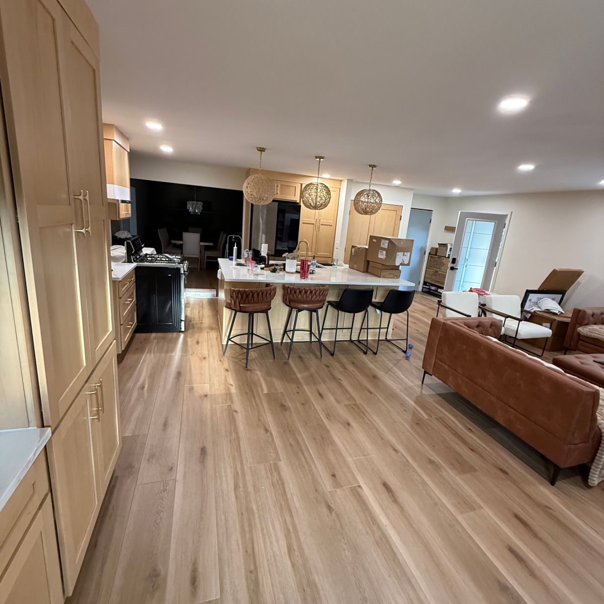 Open-plan kitchen and living room with wood floors, island bar stools, and brown sofa under recessed lights