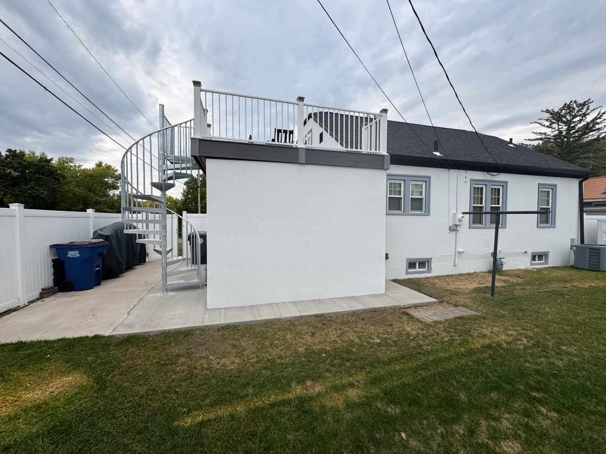White house exterior with rooftop deck, spiral staircase, and grassy yard under cloudy sky
