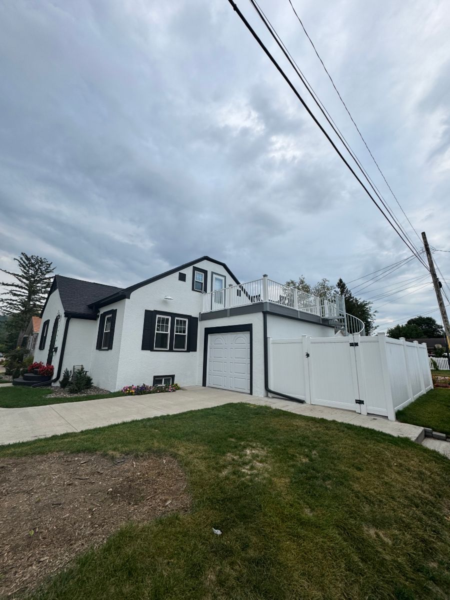 White house with black trim, garage, and fenced yard under a cloudy sky