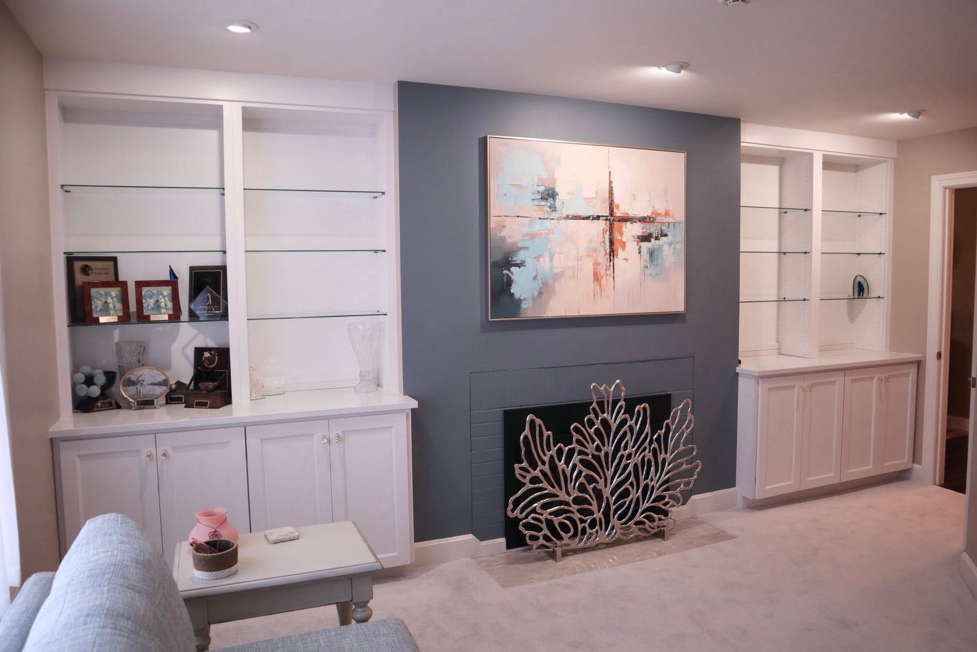 Modern living room with built-in white shelves, a dark accent wall, abstract art, and a decorative fireplace screen