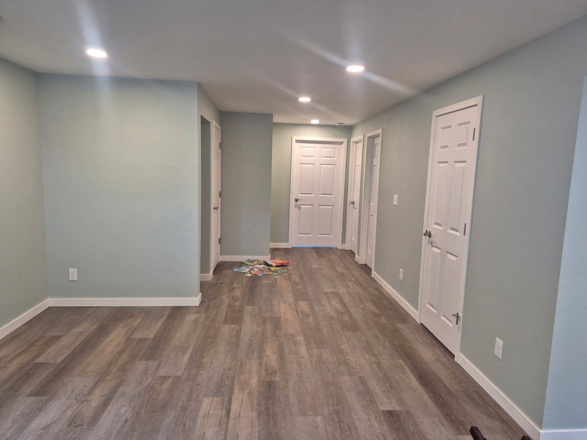 Empty hallway with gray walls, wood-look flooring, white doors, and a small toy on the floor.