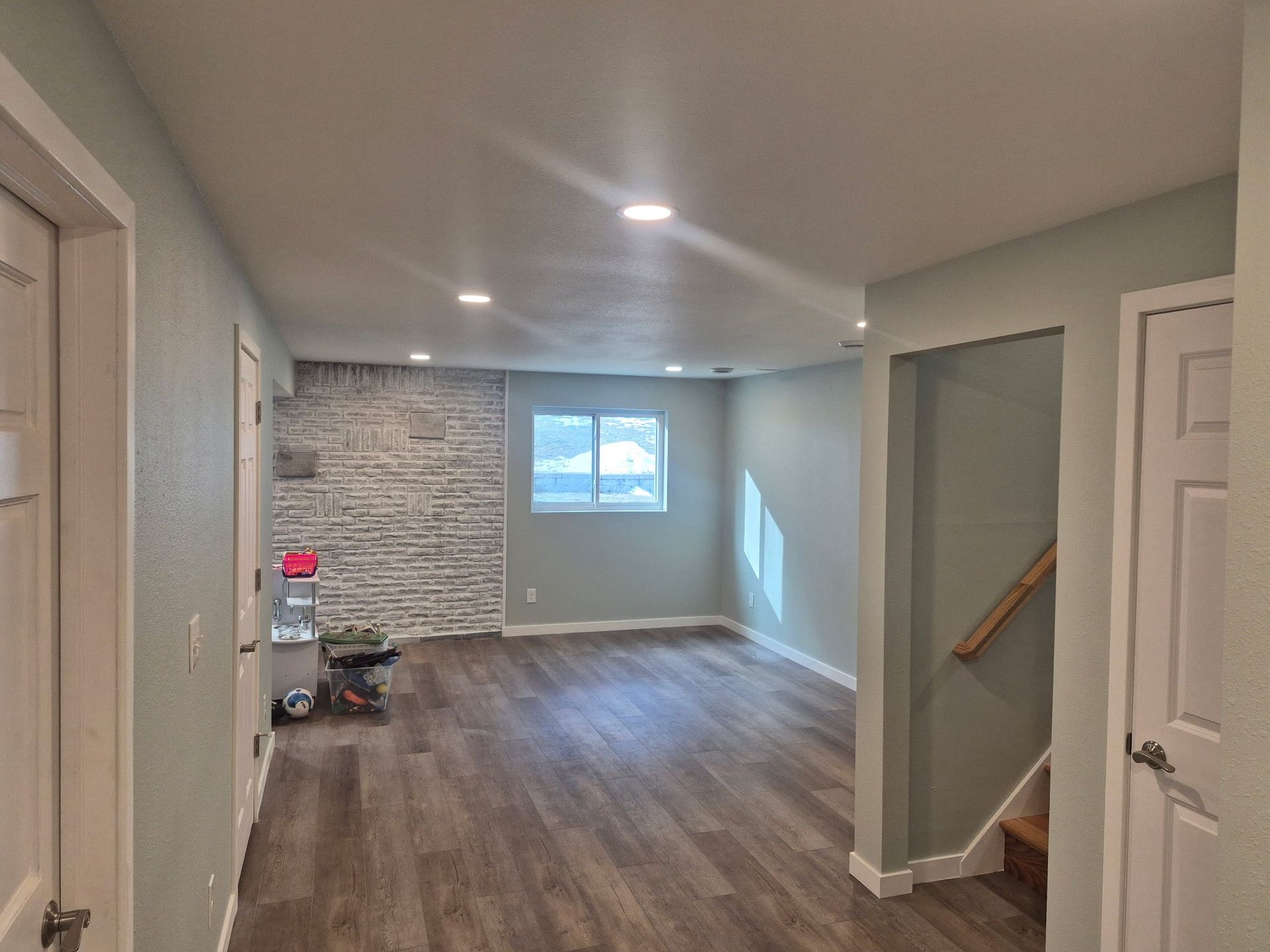 Empty living room with wood floors, white brick accent wall, and stairs visible on the right