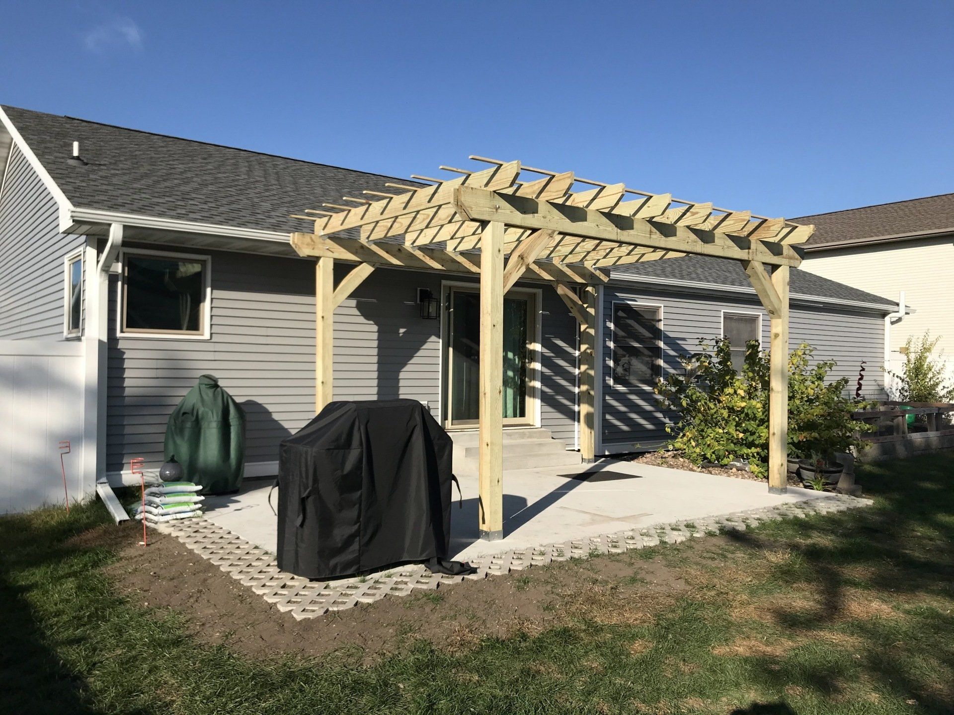 Backyard pergola attached to a gray house, with a covered grill on a patio.
