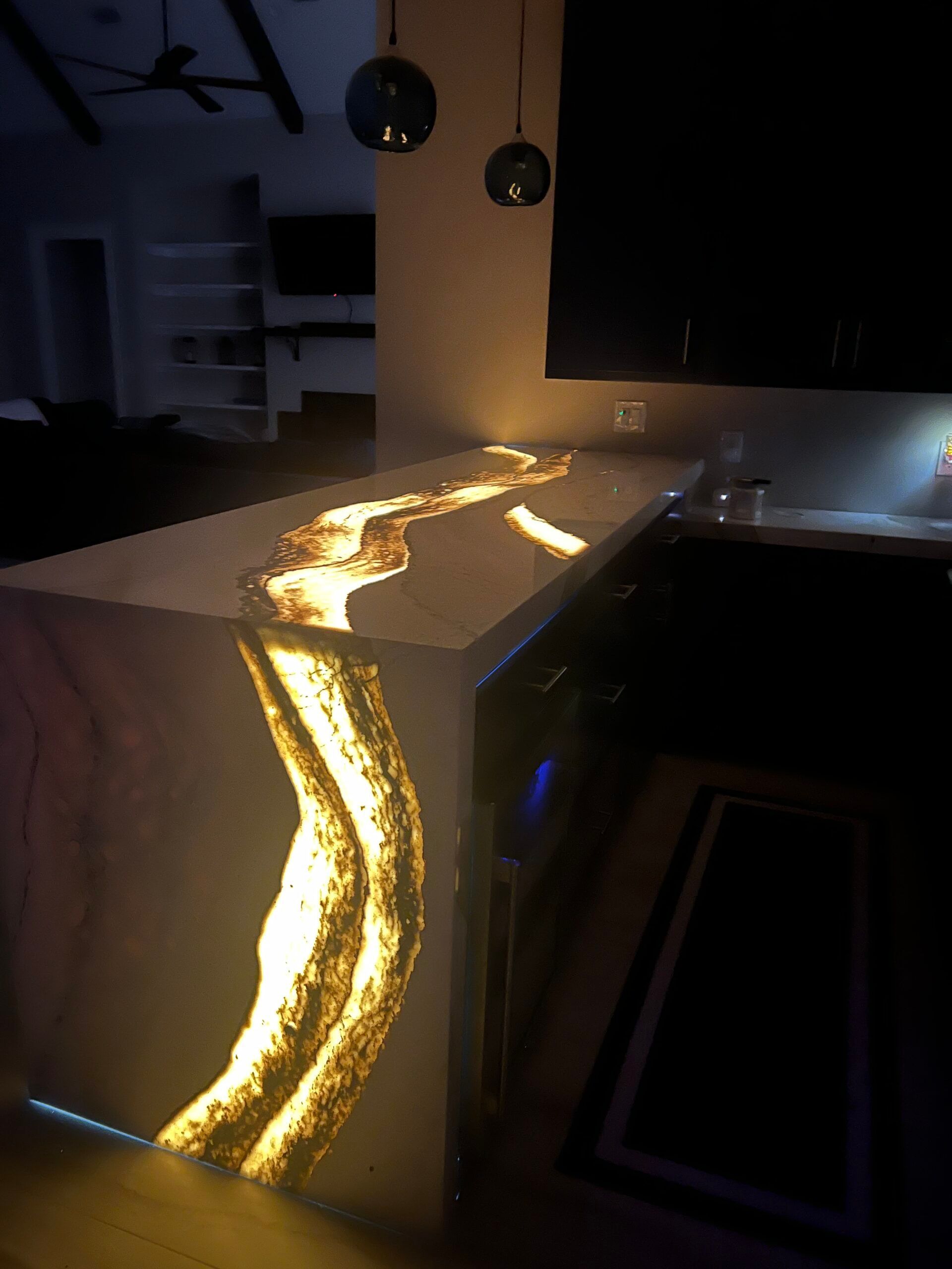 Modern kitchen island with glowing resin waterfall edge and warm gold light accents