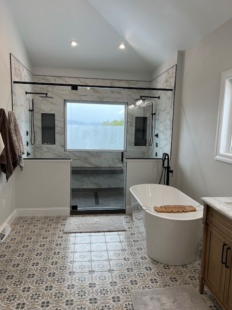 Modern bathroom with tiled floor, freestanding tub, and glass shower under a skylight
