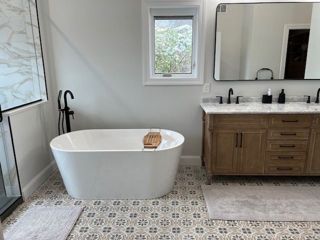Modern bathroom with freestanding tub, patterned tile floor, and wooden double vanity