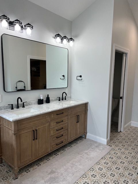Modern bathroom vanity with wood cabinets, black fixtures, large mirror, and patterned tile floor