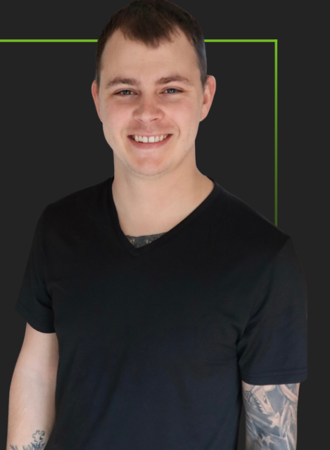 Smiling person in a black T-shirt standing against a dark background with a green outline behind them
