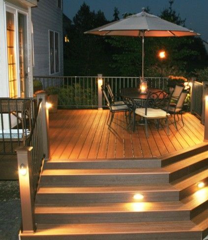 Dimly lit wooden deck with steps, outdoor table, chairs, and umbrella at dusk