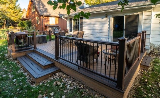Wooden deck with black railing and steps beside a house in a leafy backyard