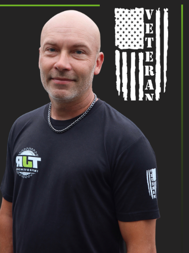 Man in black shirt with veteran logo, standing before black background with stylized American flag and “VETERAN” text