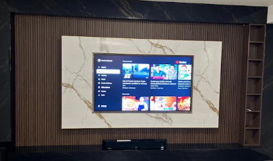 Wall-mounted TV displaying a streaming app menu against a striped accent wall with gold-framed paneling