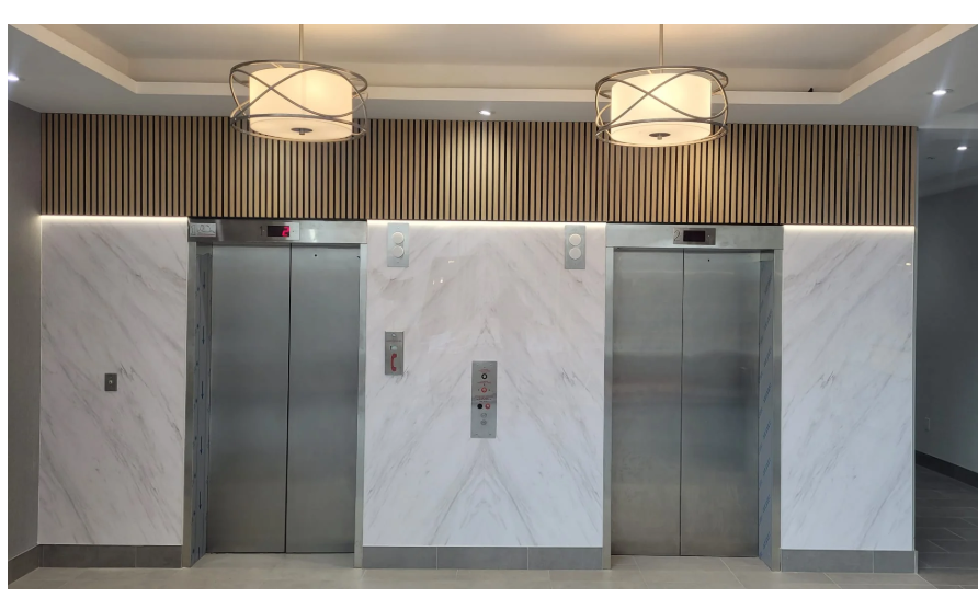 Two stainless steel elevators in a marble-walled lobby with round ceiling lights