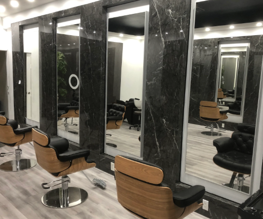 Modern barber shop interior with black marble stations, tan chairs, and mirrored styling stations