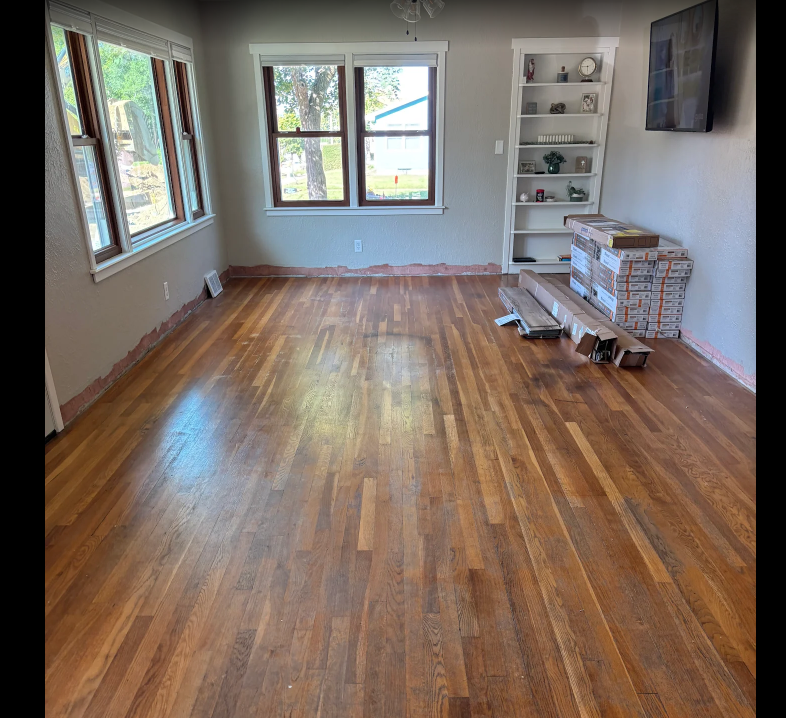 Empty room with polished hardwood floors, large windows, and a white bookshelf by the wall