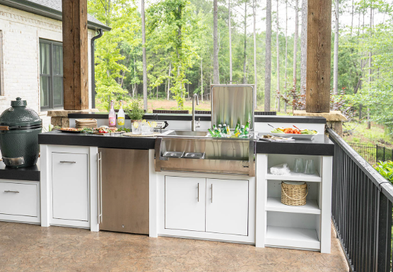 Outdoor kitchen with stainless grill, sink, and black countertop on a covered patio overlooking trees