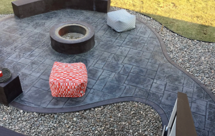 Patio with a stone fire pit, red patterned ottoman, and pebble border landscaping