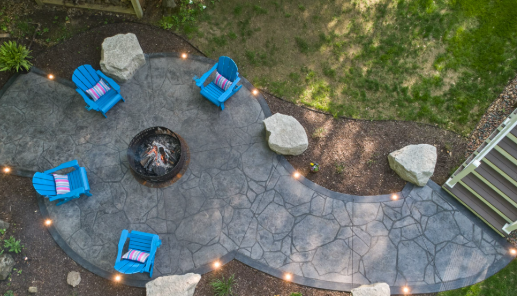 Overhead view of a stone patio with blue chairs around a fire pit and small landscape lights along the edge