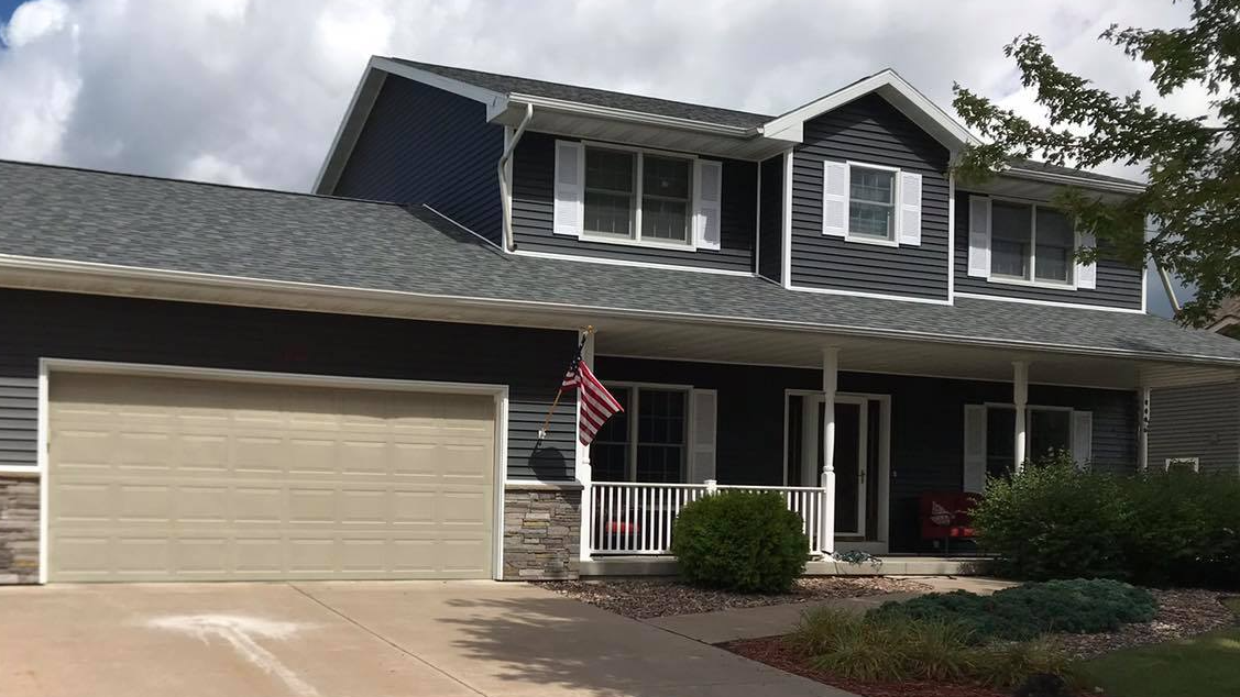 Two-story suburban house with a front porch, beige garage, and an American flag by the entrance