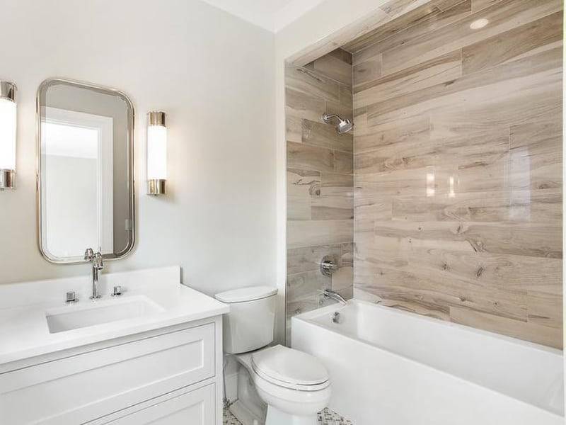 Bright bathroom with white vanity, toilet, tub, and beige wood-look shower wall