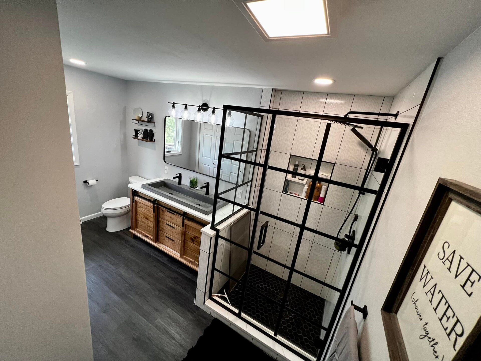 Bathroom with vanity mirror and black metal shower enclosure, plus a “Save Water” sign on the wall