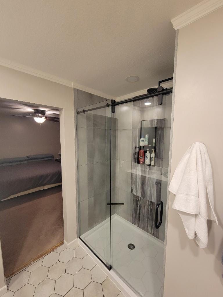 Bathroom with glass shower, hexagon tile floor, and a white towel on the wall.