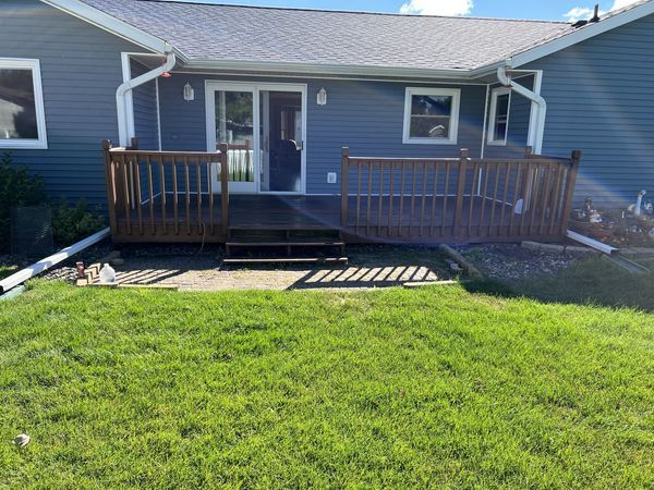 Blue house with a small wooden deck and railing overlooking a green lawn.
