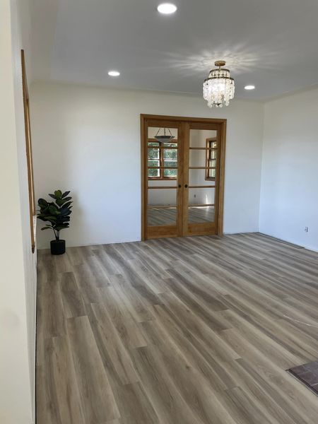 Empty modern room with wood-look flooring, recessed lights, chandelier, potted plant, and glass double doors