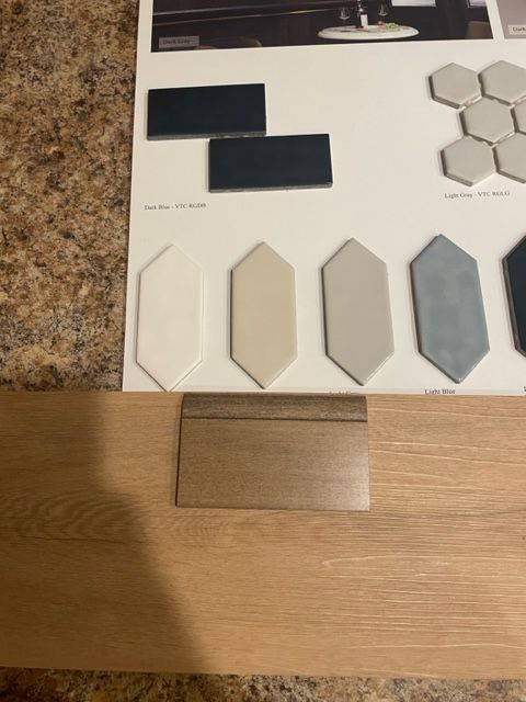 Flooring samples and tile swatches on a board beside a light wood floor plank and speckled countertop.