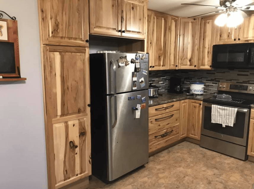 Rustic kitchen with wood cabinets, stainless steel refrigerator, and black appliances
