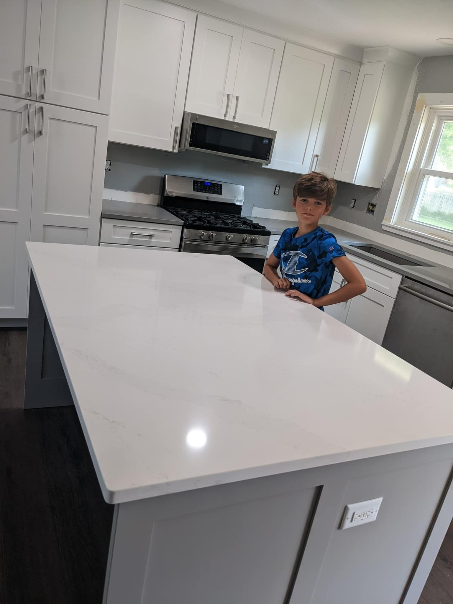Modern white kitchen with a large island and a child standing by the counter near the stove.
