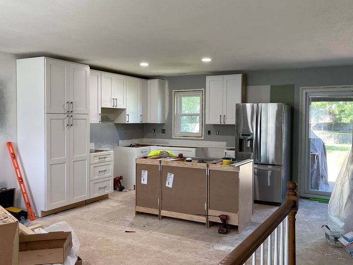 Kitchen under renovation with white cabinets, stainless fridge, and cardboard boxes on the floor