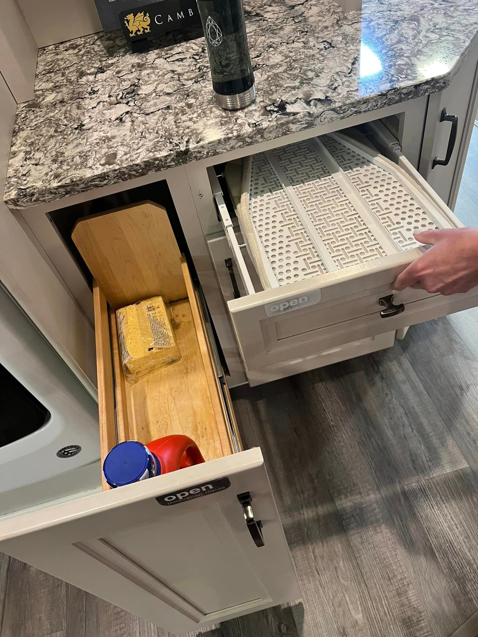 Open drawer under kitchen counter showing a white pull-out trash bin being accessed by a hand
