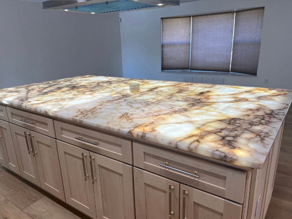Large kitchen island with marble countertop and beige cabinets in an empty room.